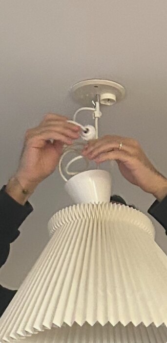 Händer installerar gammal lamppropp på vit, veckad lampskärm i taket.