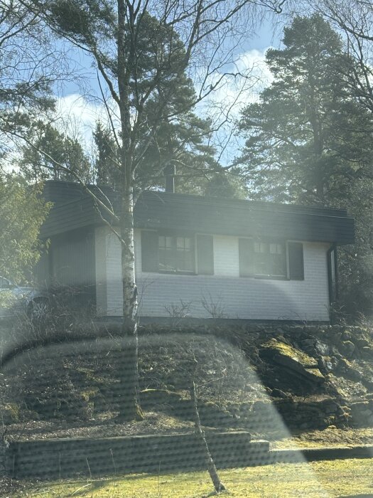En vit tegelbyggnad med mörkt tak och omgivande träd, potentiellt det nya sovrummet från garage.