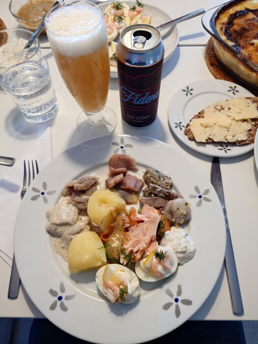 Påskbord med lax, ägg, potatis, sill och öl på ett dukat bord.