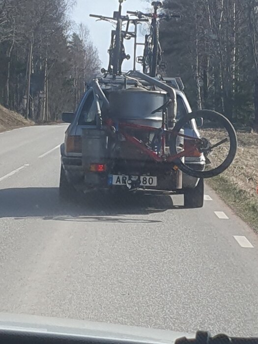 Bil på landsväg med två cyklar och en stor metallbehållare lastade på taket.