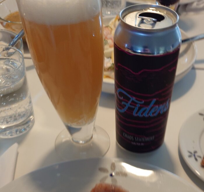 En öl från Fidens i glas bredvid en burk med etiketten "Chaos Statement", serverad på ett matbord.