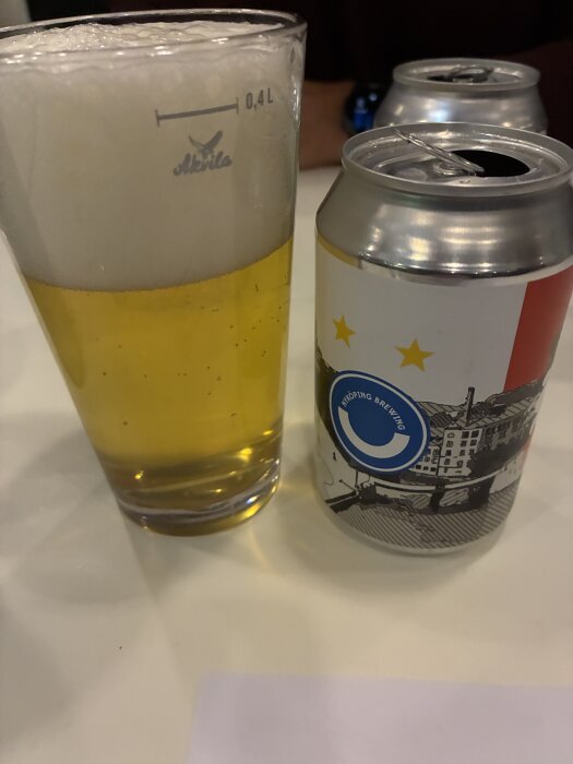 Ölglas med skum bredvid en ölburk med etikett som visar en stadsmotivetikett.