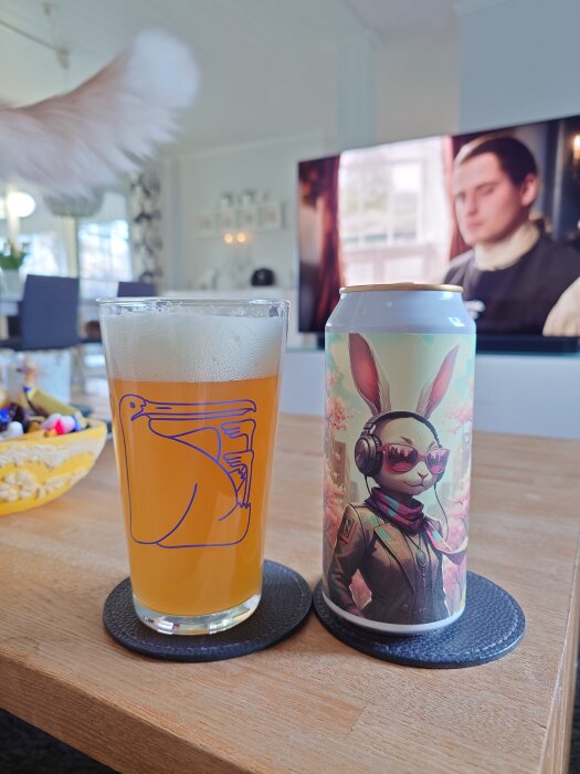 En öl i glas med pelikanlogga och burk med vårigt kaninmotiv på ett bord, TV i bakgrunden.