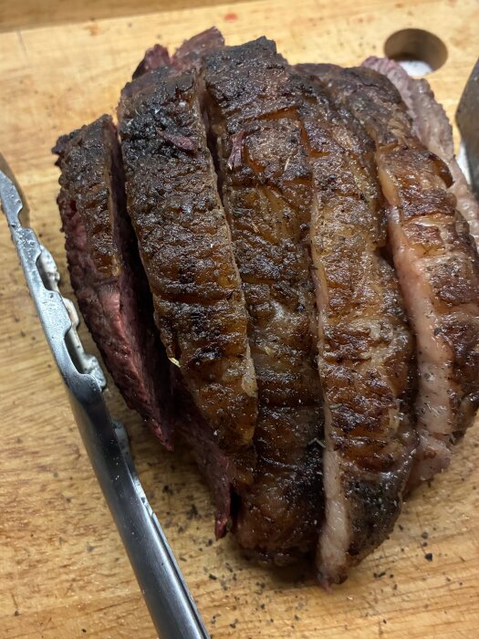 Skivad picanha på en träskärbräda med en köttång bredvid.