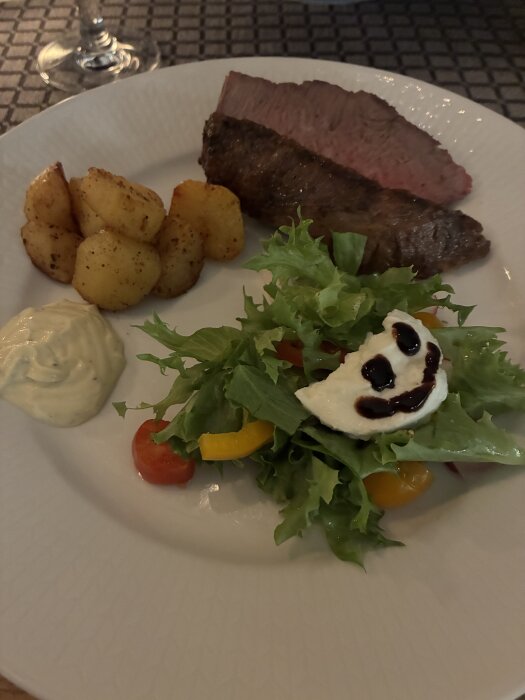 Skivad picanha med rostade potatisar, sallad med paprika och mozzarella, en krämig sås och ett glas vin i bakgrunden.