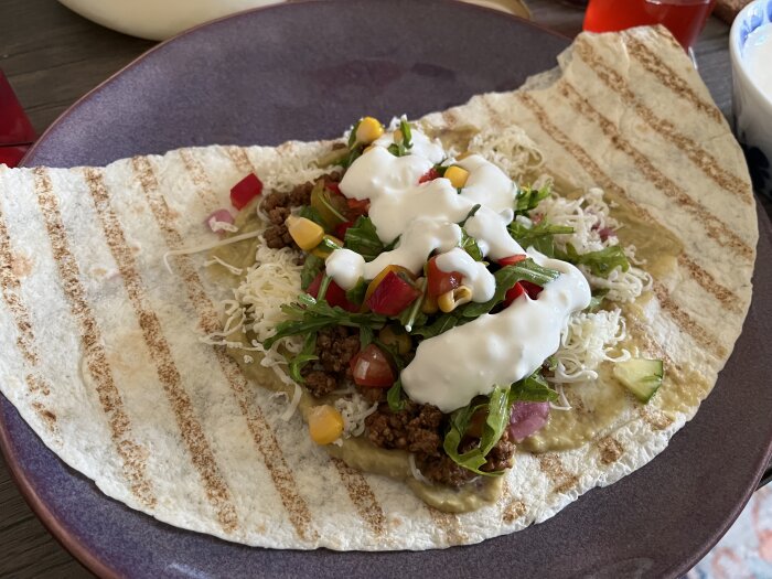 Tortilla fylld med köttfärs, grönsaker, ost och sås, serverad på en tallrik, redo att vikas till påsktacos.