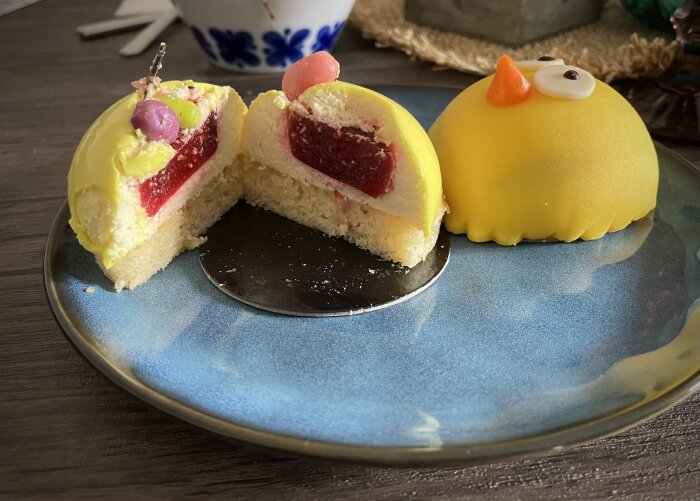 Påsktårtor med gul glasyr, fyllda med hallonsylt och passionsfruktsmousse, serverade på ett blått fat. En tårta har dekoration som en kyckling.