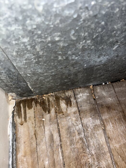 Fuktiga fläckar på trägolv nära ventilationskanal i kallvind, möjligt tecken på kondensläckage.