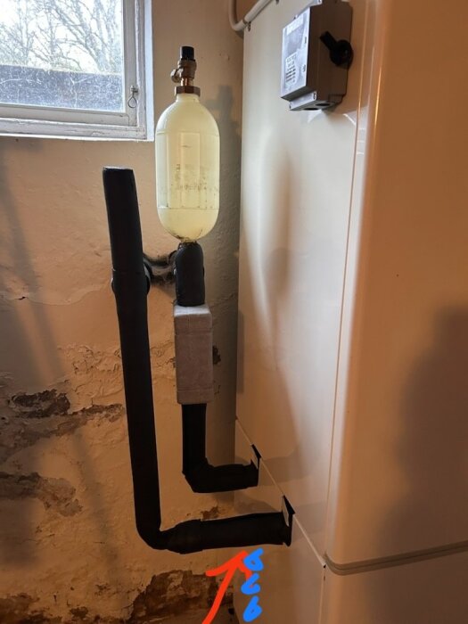 Bilden visar en bergvärmepump från NIBE med rostiga gängor och ny isolering, där en köldbärarflaska läcker vätska som rinner in i pumpens skal.