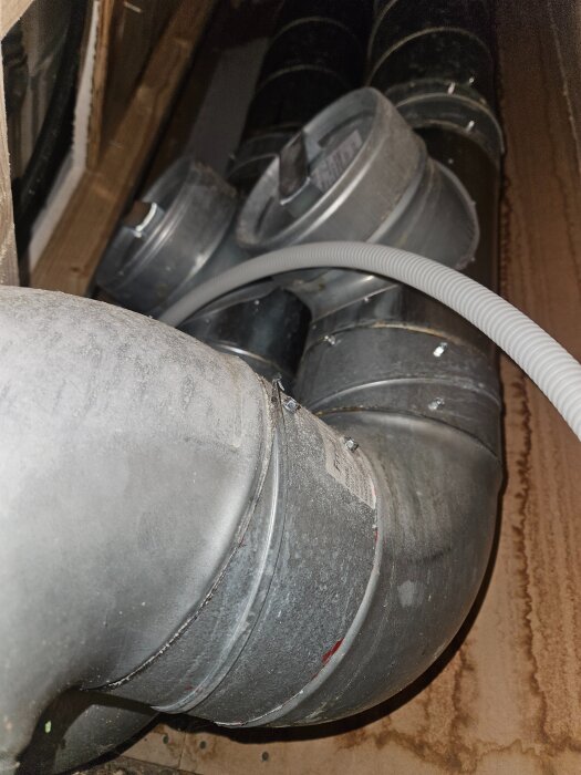 Ventilationsrör i ett trångt schakt med gipsskivor på sidorna och en elkabel i förgrunden.