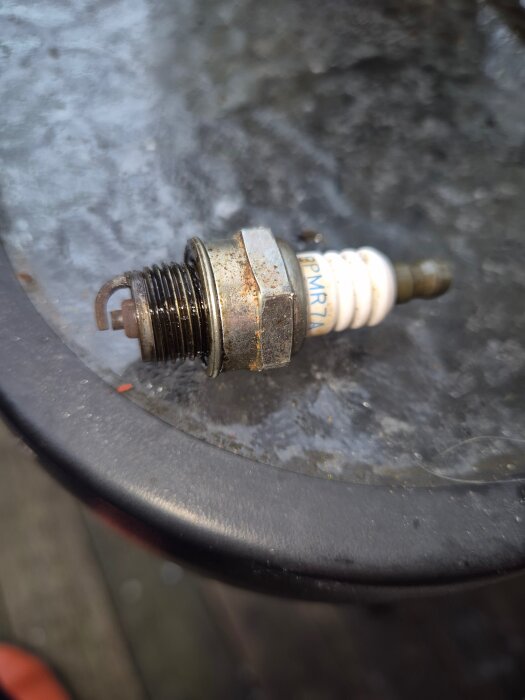 Gammal, använd tändstift ligger på ett bord med metallisk yta.