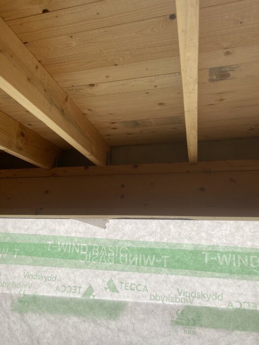 Byggprojekt för bastu, oskyddat tak med synliga takbjälkar och vindskyddsmaterial märkt "T-WIND BASIC" delvis installerat.