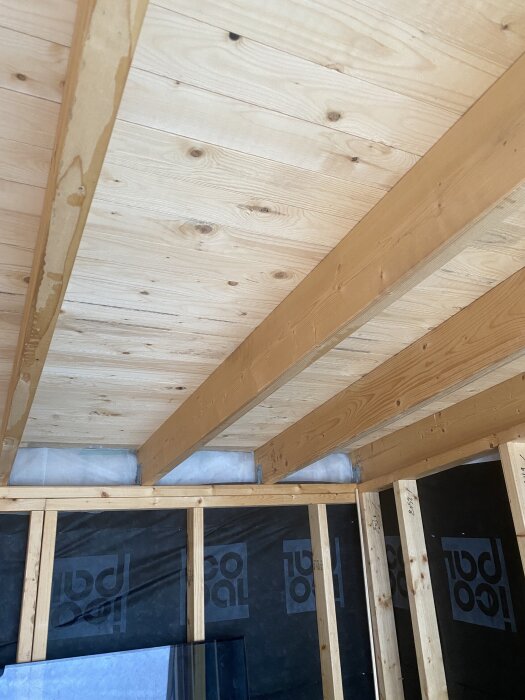 Interiör av oavslutat bygge med träbalkar och takreglar, del av pågående bastuprojekt, synliga byggmaterial i bakgrunden.