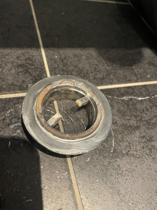 Sliten och rostig metallbricka placerad på ett mörkt golv av kakelplattor.