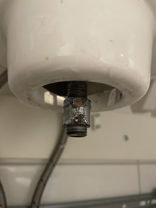 Närbild på ett metallrör med gängor under ett vitt handfat, visar tecken på rost och slitage.