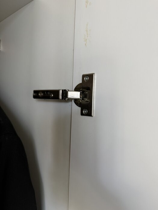 Metallgångjärn monterat på insidan av en vit skåplucka.