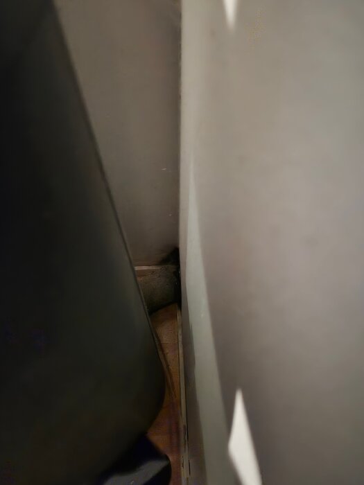 Braskaminens friskluftsrör intill en vit vägg, möjlig mögelpåverkan synlig. Röret måste åtkommas för inspektion och eventuell åtgärd.