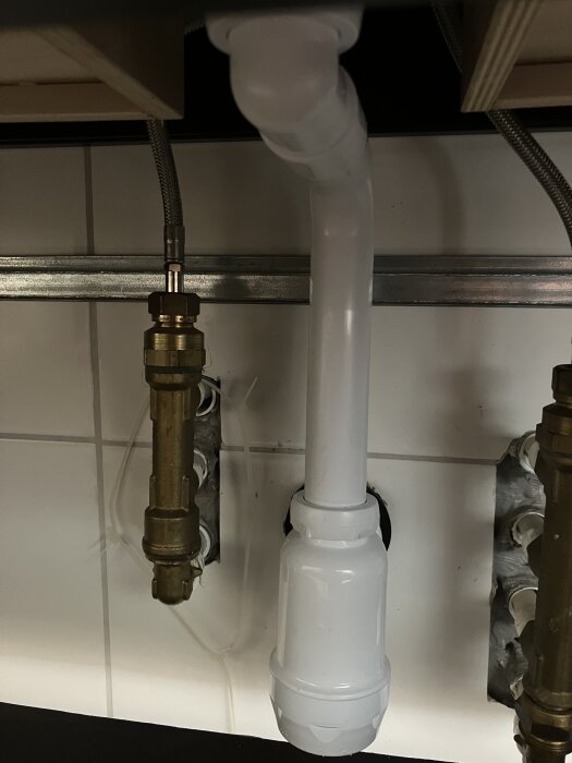 Nytt vitt vattenlås installerat under diskbänk med anslutna rör och kopplingar.
