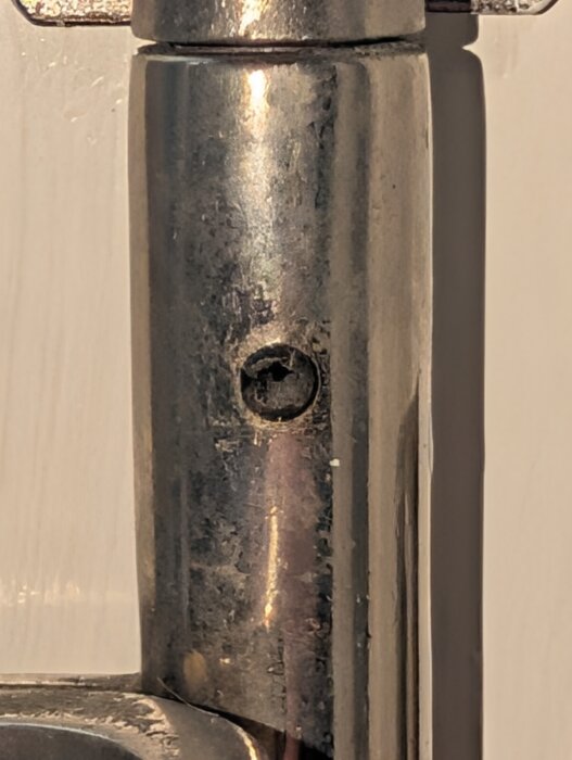 Närbild av ett metallgångjärn med hål för en insexskruv eller rörsprint, där en kapad skruv kan ha satts i stället.