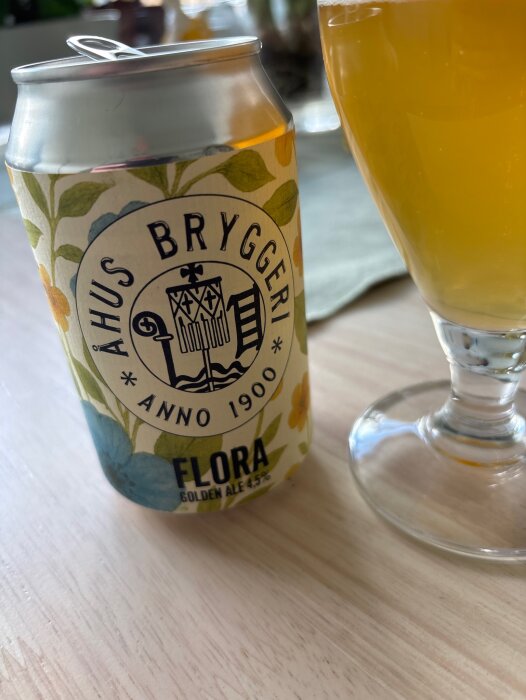 En burk Flora Golden Ale från Åhus Bryggeri på ett bord bredvid ett glas med öl.