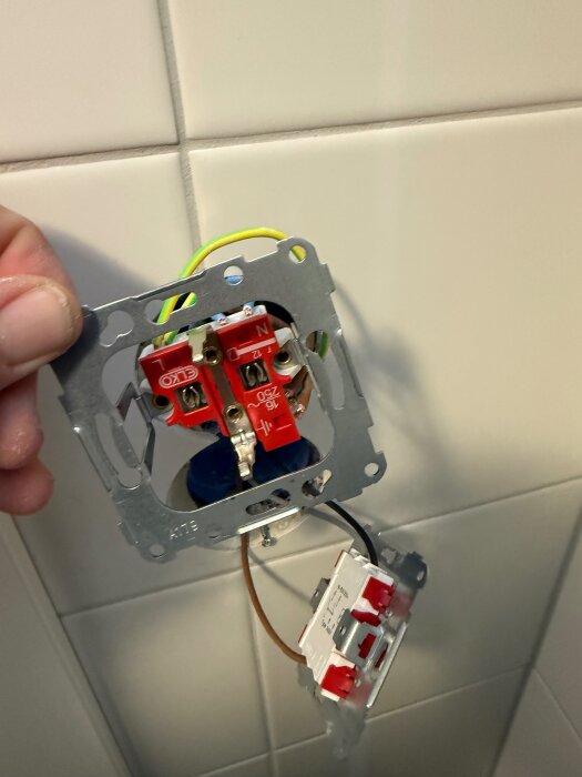 Elektrisk kopplingsinstallation med synliga jord- och fasledningar framför kaklat väggparti.