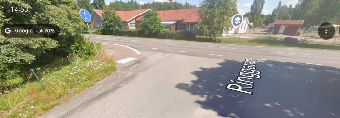 Street view-bild av en korsning med vägskylt, vegetationen längs vägen och byggnader i bakgrunden, markerad med "Ringgatan".