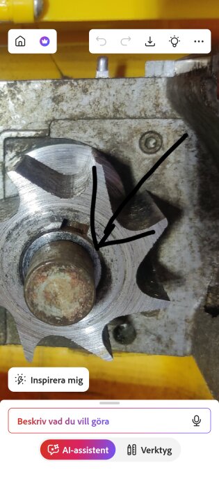 Närbild av en bronshylsa och kugghjul som pekas ut av en svart pil, omgiven av metalliska komponenter och en gul bakgrund.