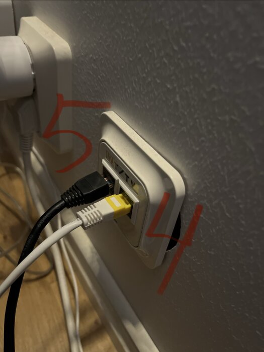 Vägguttag med två nätverkskablar anslutna, en svart och en vit. Röda markeringar visar "5" och "4" vid respektive kabel.