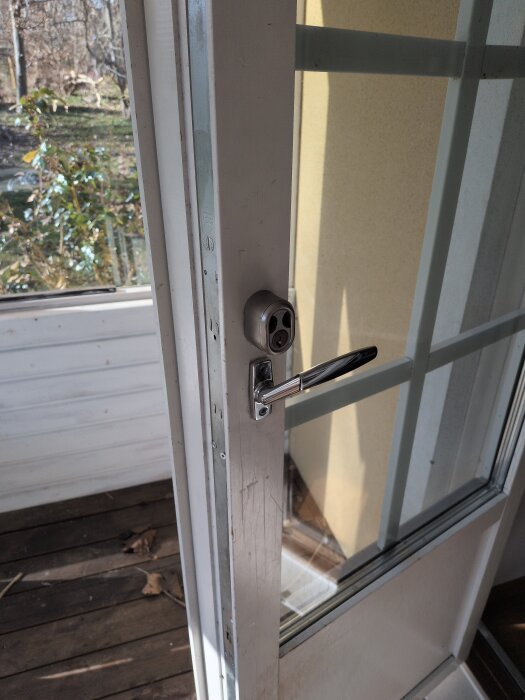 Öppen vit dörr med glasrutor, ledande ut mot en veranda med trädeck.