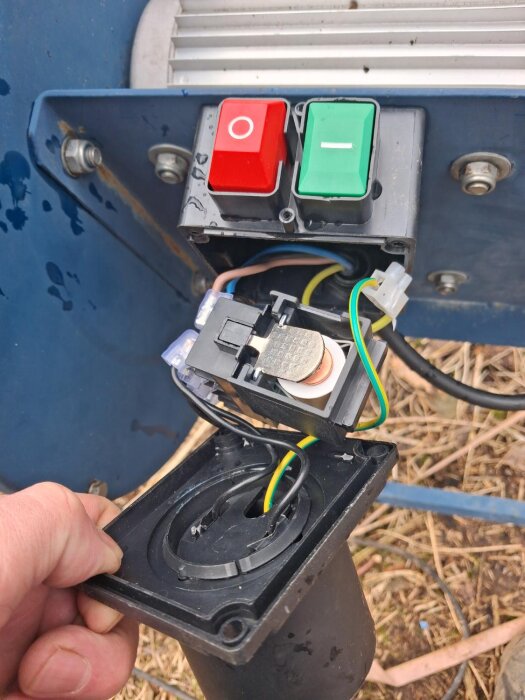 Öppen panel med inre kopplingar till en vedkaps strömbrytare, visar röd och grön knapp, kablar och elektriska komponenter.