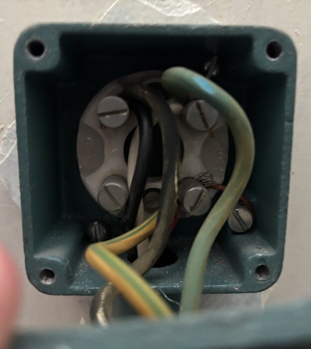 Öppen elbox med flera färgade kablar och skruvar, monterad i ett vägguttag.