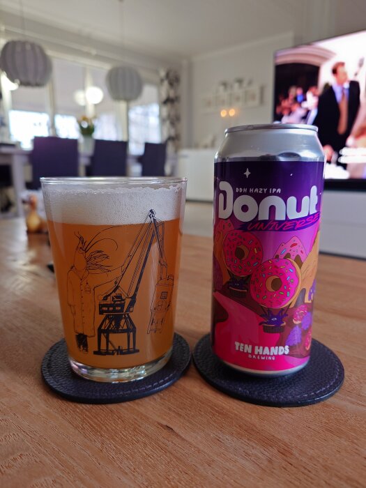 Ett glas öl och en burk med etiketten "Donut Universe" från Ten Hands Brewing, placerade på ett bord i ett vardagsrum.