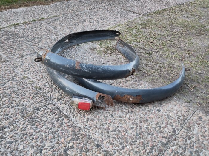 Rostiga cykelskärmar ligger på marken redo för renovering i ett lådcykelprojekt.