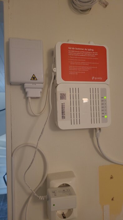Fiberanslutningsdosa och modem monterade på vägg med flera kablar anslutna, inklusive strömkabel och nätverkskabel.