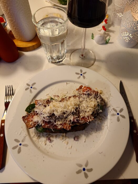 Seglartoast på tallrik med oxfilé, béarnaisesås, rödlök, pepparrot, babyspenat, tomater och riven parmesan. Rödvinsglas och vattenglas bredvid.