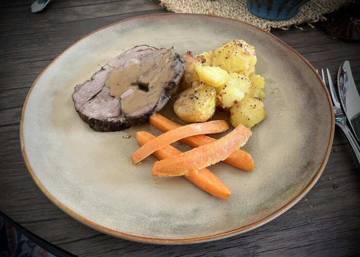 Tallrik med lammstek i sås, smörslungade morötter och ugnstekt potatis med vitlök, rosmarin och svartpeppar.