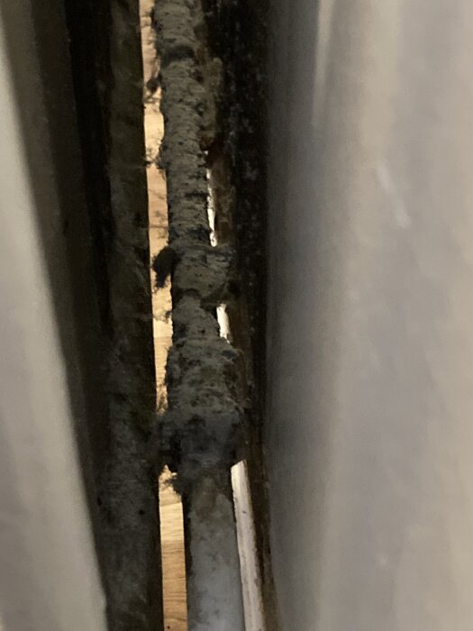 Gammelt rør bagved radiator, dækket med mørk isolering, muligvis asbest eller gurmassa. Diskuteres om beskyttelse mod varmetab.