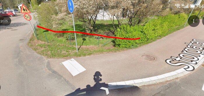 Gatulandskap med röda linjer som markerar en förslag på häckens placering längs vägen, med vägskyltar och grönska i bakgrunden.
