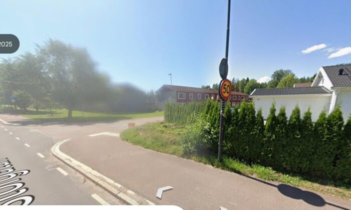 Gata med häck vid trottoarkant och ett hastighetsskylt 50. Rött tegelhus i bakgrunden.