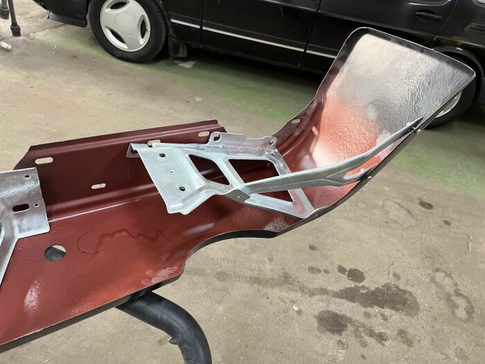 En metallram i röd och silverfärg, placerad på ett stativ i ett garage, med en bil i bakgrunden.