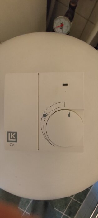 Termostat från LK Systems med justeringsratt och tryckmätare, del av vattenburet golvvärmesystem i ett hus.