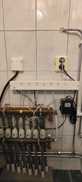 Fördelningscentral med kablar och anslutningar för golvvärmesystem från LK Systems, monterad på kakelvägg.