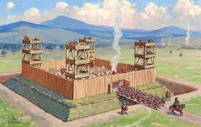 Romerskt fort med vakttorn, tält innanför träbarrikader, romerska soldater marscherar in, landskap med berg i bakgrunden.