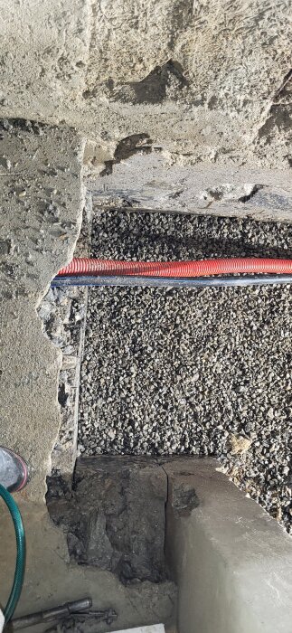 Sprucken betongyta med röd kabel i gruslager, reparationer pågår.