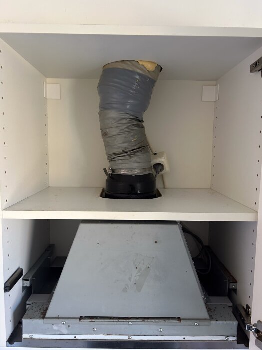Felinstallerad köksfläkt i ett skåp, med en grå tejpad ventilationstumlare som leder till husets kanal; planerat ombyggnad för recirkulering.