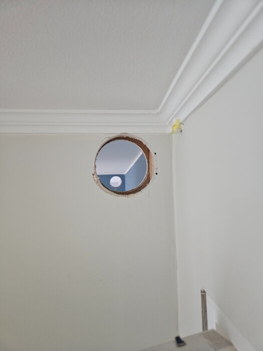 Hål i väggen nära taket, förberett för installation av ett 125 mm ventilationsrör mellan rum.
