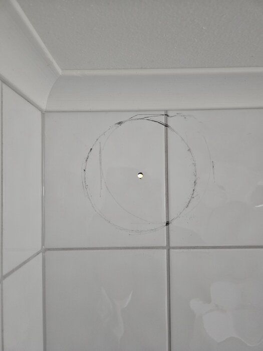 En vägg av vita kakelplattor med ett litet borrat hål i mitten av en större markerad cirkel på ytan.