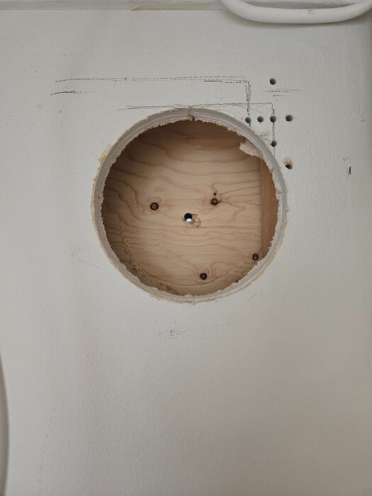 Hål i vägg för ventilationsrör mellan rum, med mindre borrhål runt det större hålet.
