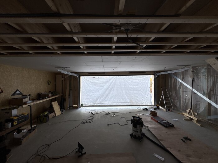 Ett garage under konstruktion, med synligt takstolar, installationsutrustning och verktyg utspridda. En HEB220 stålbalk stödjer taket.