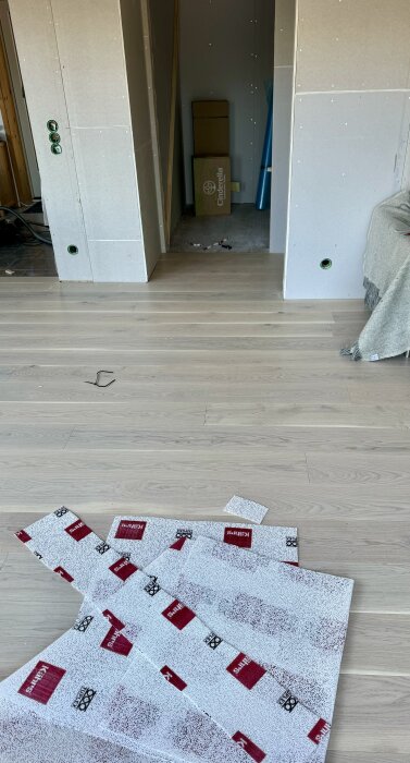 Nylagd ljust trägolv i ett rum, med några skyddspapper och kartonger i bakgrunden. Vägghyllor och verktyg är inte synliga.